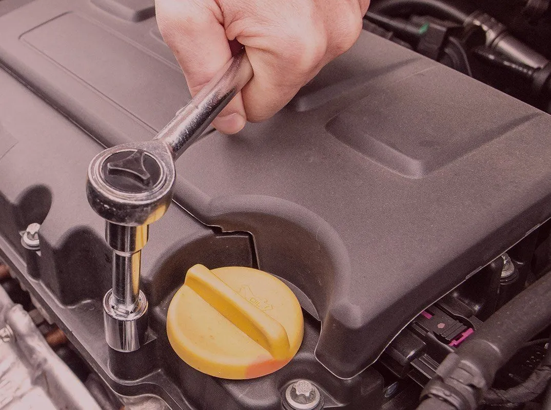 A hand turning a socket wrench over an engine, beside the yellow oil filler cap.
