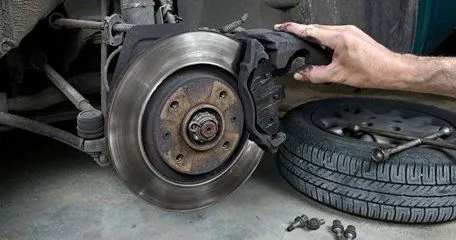 A brake disc and caliper with the wheel off and the tyre laid on the floor beside it.