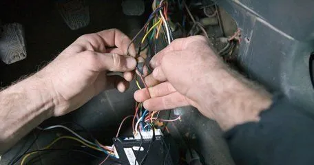 Two hands working on a wiring loom behind a dashboard.