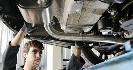 A technician under a raised car, looking along the exhaust.